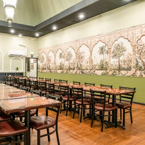 Dining room at India Palace with long tables, chairs, and a wall mural depicting Indian architecture and nature.