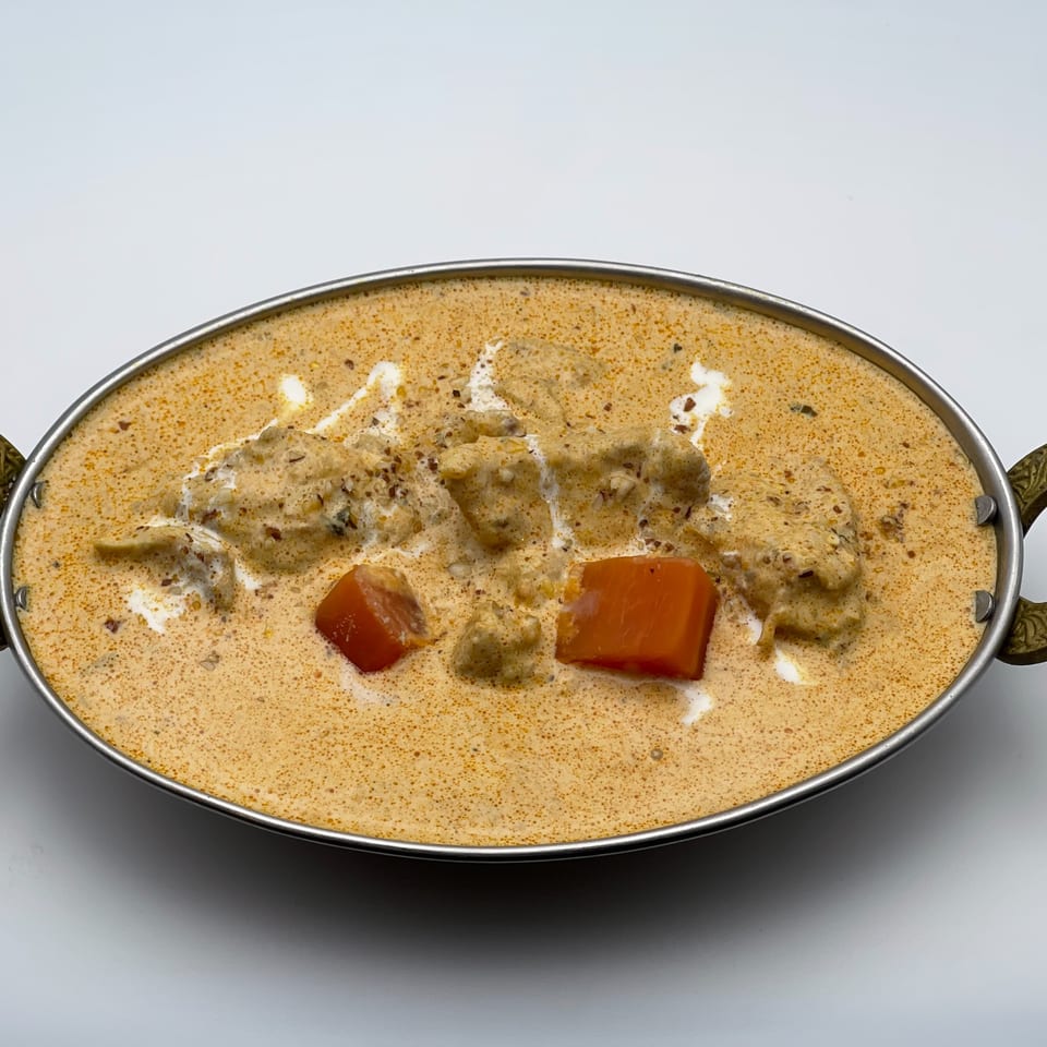 Creamy Indian chicken curry with red bell peppers, served in a metal bowl.