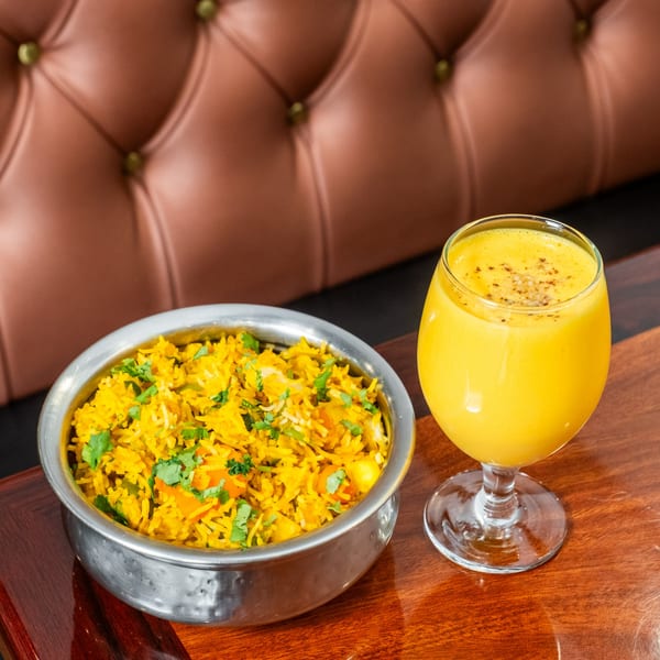 Indian Palace's vegetable biryani in a metal bowl with a mango lassi on a wooden table.