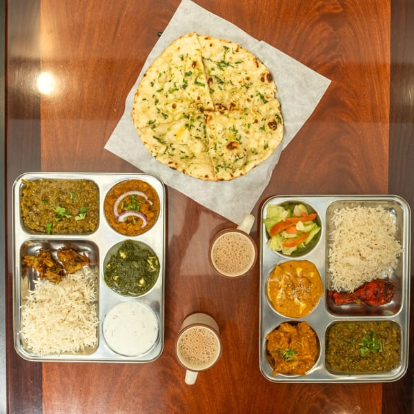 Overhead view of two Indian thali platters with various dishes, naan bread, and two cups of chai.
