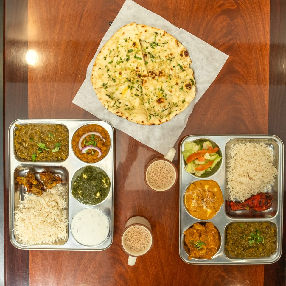 Overhead view of two Indian thali platters with various dishes, naan bread, and two cups of chai.