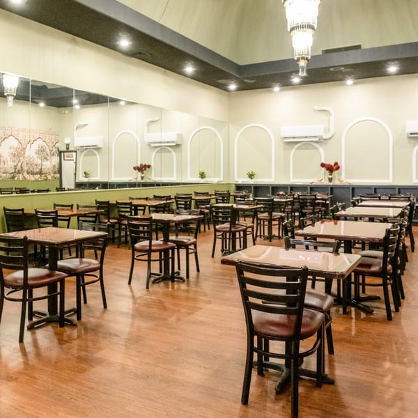 Empty dining room at India Palace with many tables and chairs, light green walls, and wood floors.