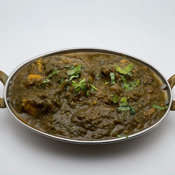 Palak Paneer, a vibrant green Indian spinach and cheese curry, garnished with fresh cilantro in a metal serving dish.
