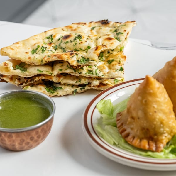 Indian Palace naan bread, samosas on lettuce, and green chutney on a white surface.