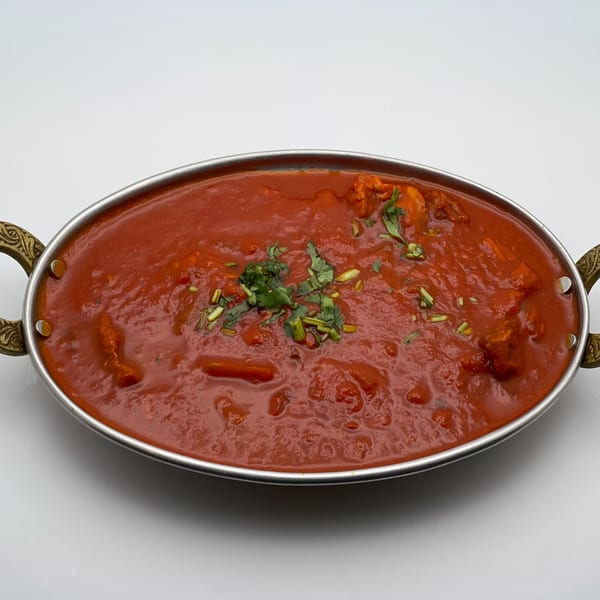 A metal serving dish filled with red Indian curry, garnished with fresh green herbs.