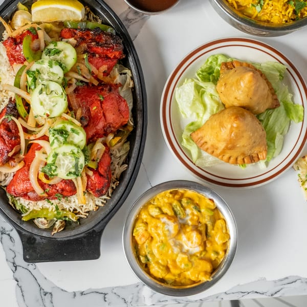 A vibrant Indian meal featuring chicken tikka, samosas, and a creamy curry on a marble table.