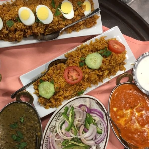 Two plates of Indian biryani rice with eggs, along with dal, curry, and onion salad.