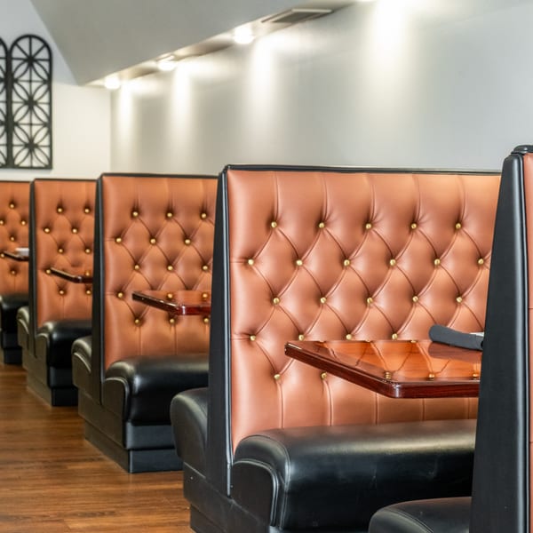 Row of empty brown and black tufted booths with wooden tables in India Palace restaurant.