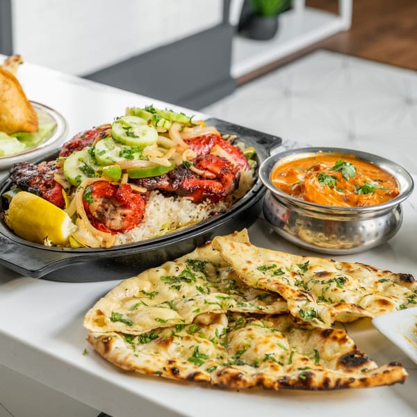 A vibrant Indian meal featuring chicken tikka, rice, naan, and curry on a white table.