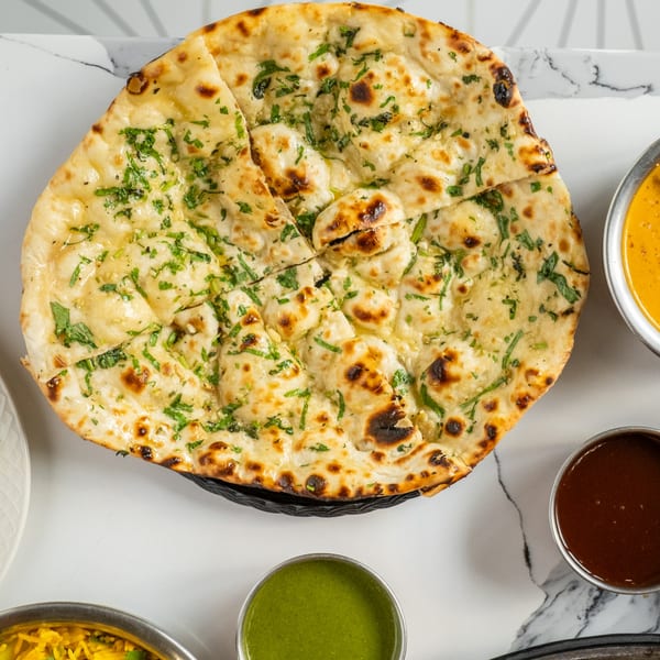 Garlic naan bread, cut into pieces, with cilantro and butter, alongside Indian sauces.