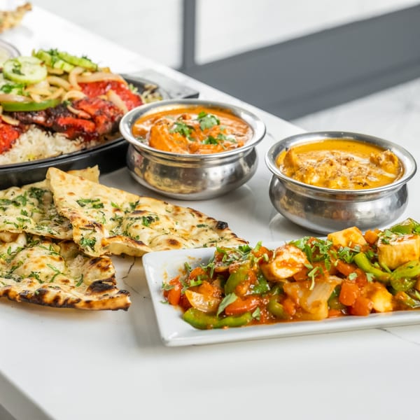 A spread of Indian dishes including naan, curries in metal bowls, and a vegetable stir-fry.