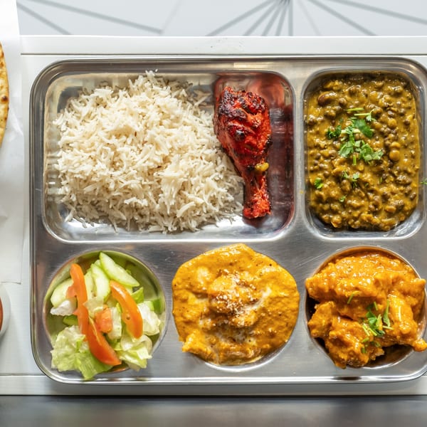 An Indian thali with rice, tandoori chicken, dal, butter chicken, paneer, and a side salad.