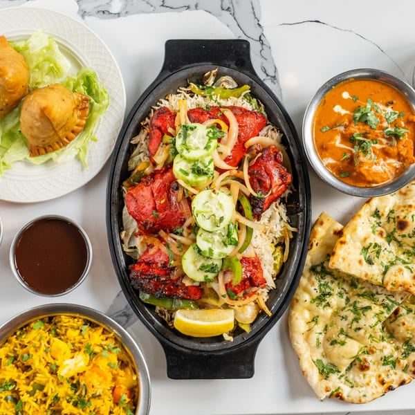 An Indian feast with chicken tikka, biryani, samosas, butter chicken, naan, and yellow rice.