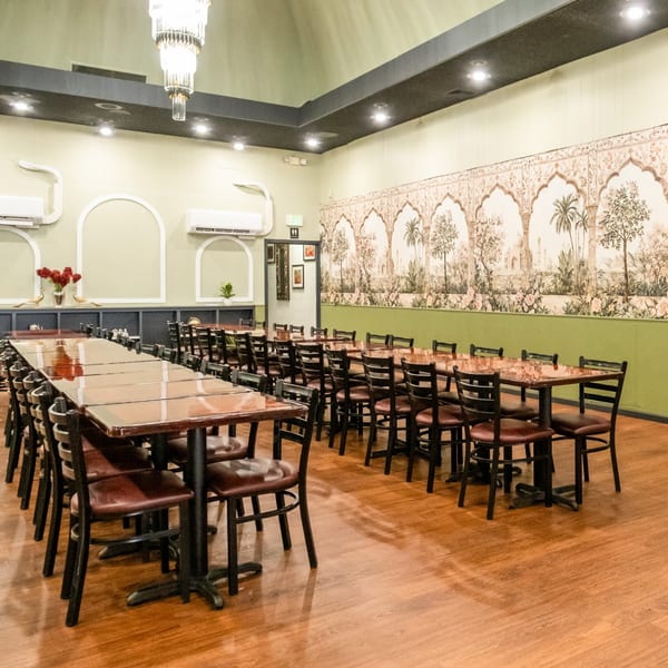 India Palace dining room with long tables, brown chairs, and a mural of Indian architecture and trees.