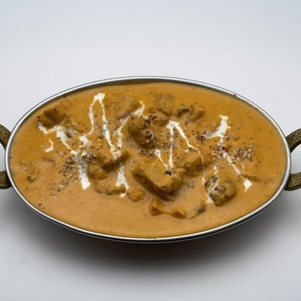 Indian butter chicken in a metal serving dish, garnished with cream and spices.