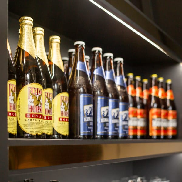 Rows of Indian beer bottles, including Flying Horse Royal Lager and Himalayan, displayed on a shelf.