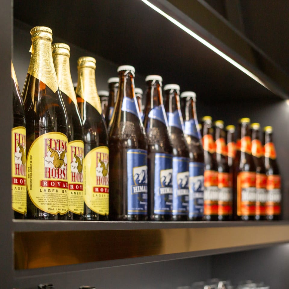 Rows of Indian beer bottles, including Flying Horse Royal Lager and Himalayan, displayed on a shelf.