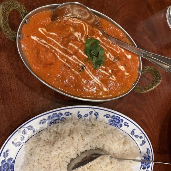 A metal serving dish of Indian butter chicken with cilantro and a side of white rice.
